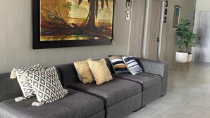 A modern living room with a grey sectional sofa, a large abstract painting, and a potted plant. - Hotel Panorama  (El Banco)