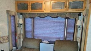 A compact RV interior with two armchairs, a small kitchenette, and a refrigerator. - Spacious Clean RV Camper (Palm Bay)