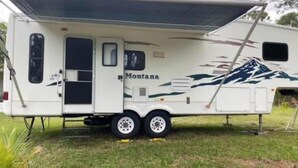 A white RV with a 'Montana' decal and a mountain design, featuring a covered living area and a small kitchen. - Spacious Clean RV Camper (Palm Bay)