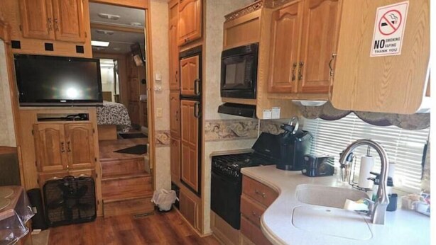 A compact RV kitchen with wooden cabinets, a stove, microwave, and a sink. - Spacious Clean RV Camper (Palm Bay)