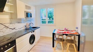 Une cuisine compacte équipée d’un four encastré, d’un lave-linge et d’un coin repas avec une table dressée pour deux personnes.