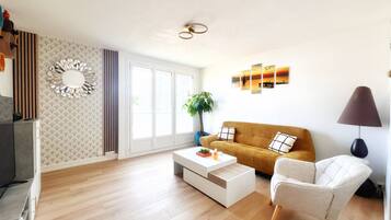 A modern living room with a sofa, a chair, a coffee table, and a lamp. There is a large window with a view of the outside.