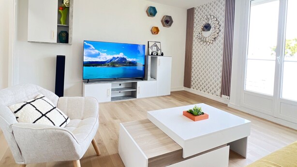 Un salon moderne avec un téléviseur à écran plat, un canapé blanc, un divan jaune et une table basse.