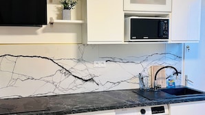 Une cuisine compacte avec des meubles blancs, un plan de travail noir, un four à micro-ondes, un évier, un lave-vaisselle et un lave-linge.