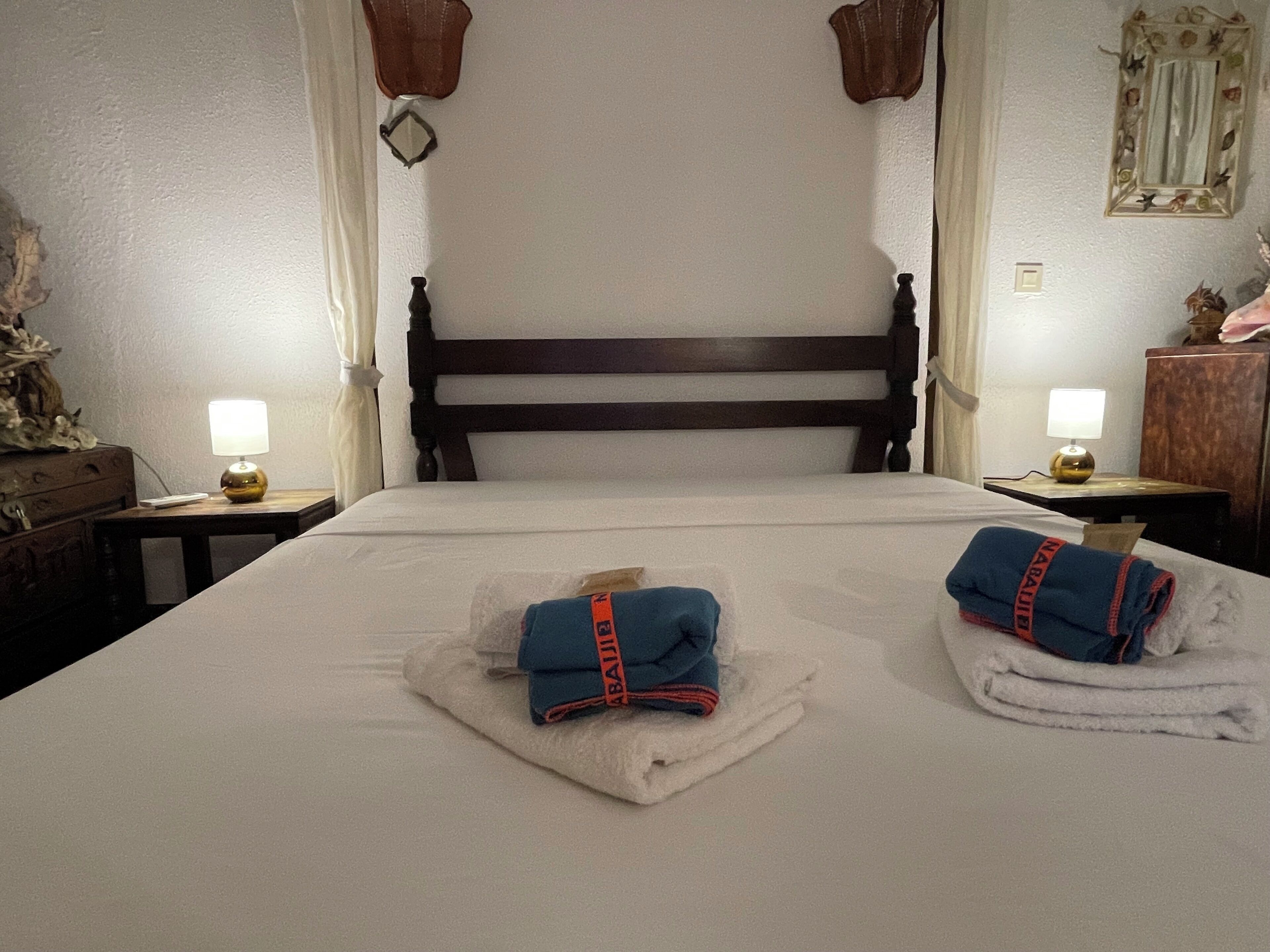 Une chambre d’hôtel avec un grand lit, deux tables de chevet avec des lampes, une tête de lit en bois et un miroir décoratif au mur.
