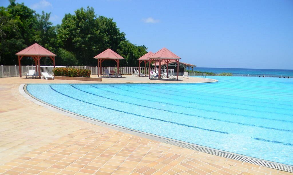 A swimming pool with lounge chairs and gazebos, surrounded by a tiled deck and a view of the ocean.
