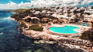 A coastal resort with a large turquoise pool surrounded by a rocky shoreline and a residential area in the background. - Anse des Rochers Beach & Pool Resort (Saint-François)