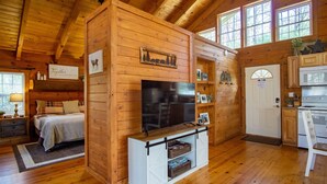 Een gezellig chaletinterieur met een bed, televisie, houten planken en een keukenhoek.