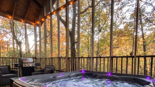 Een jacuzzi met waterstralen, omringd door houten terrasmeubels, onder een overdekt gebied met lichtslingers.