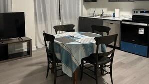 Una cocina moderna con armarios oscuros, microondas y estufa. Hay una mesa de comedor con sillas y un televisor sobre un mueble.