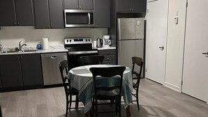 Una cocina moderna con armarios oscuros, microondas, estufa y refrigerador. Hay una mesa de comedor con sillas y una pequeña mesa redonda con cubierta de mármol.