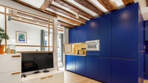 Una cocina moderna con armarios azules, horno empotrado y televisor sobre un mueble blanco.