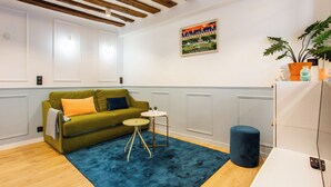 Una sala moderna con un sofá verde, un tapete azul, una mesita redonda pequeña y un reposapiés azul.