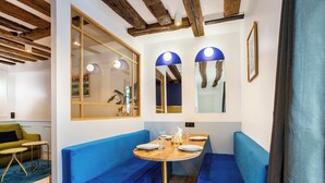 Un área de comedor con asientos tapizados en azul, una mesa de madera y un ventanal con vistas a la ciudad.