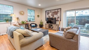 A living room with two sofas, a coffee table, a TV, and a large window with a view of the backyard. - TWO townhomes for your giant group! (Corvallis)