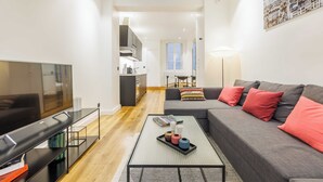 A modern living room with a flat-screen TV, a sofa with red cushions, a coffee table with books and a tray, and a dining area in the background. - Cosy Apartment - 1br/4p - Near Champs-elysees (Paris)