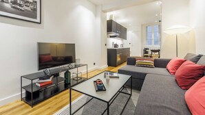 A modern living room with a flat-screen TV, a sofa, a coffee table, and a kitchen area in the background. - Cosy Apartment - 1br/4p - Near Champs-elysees (Paris)
