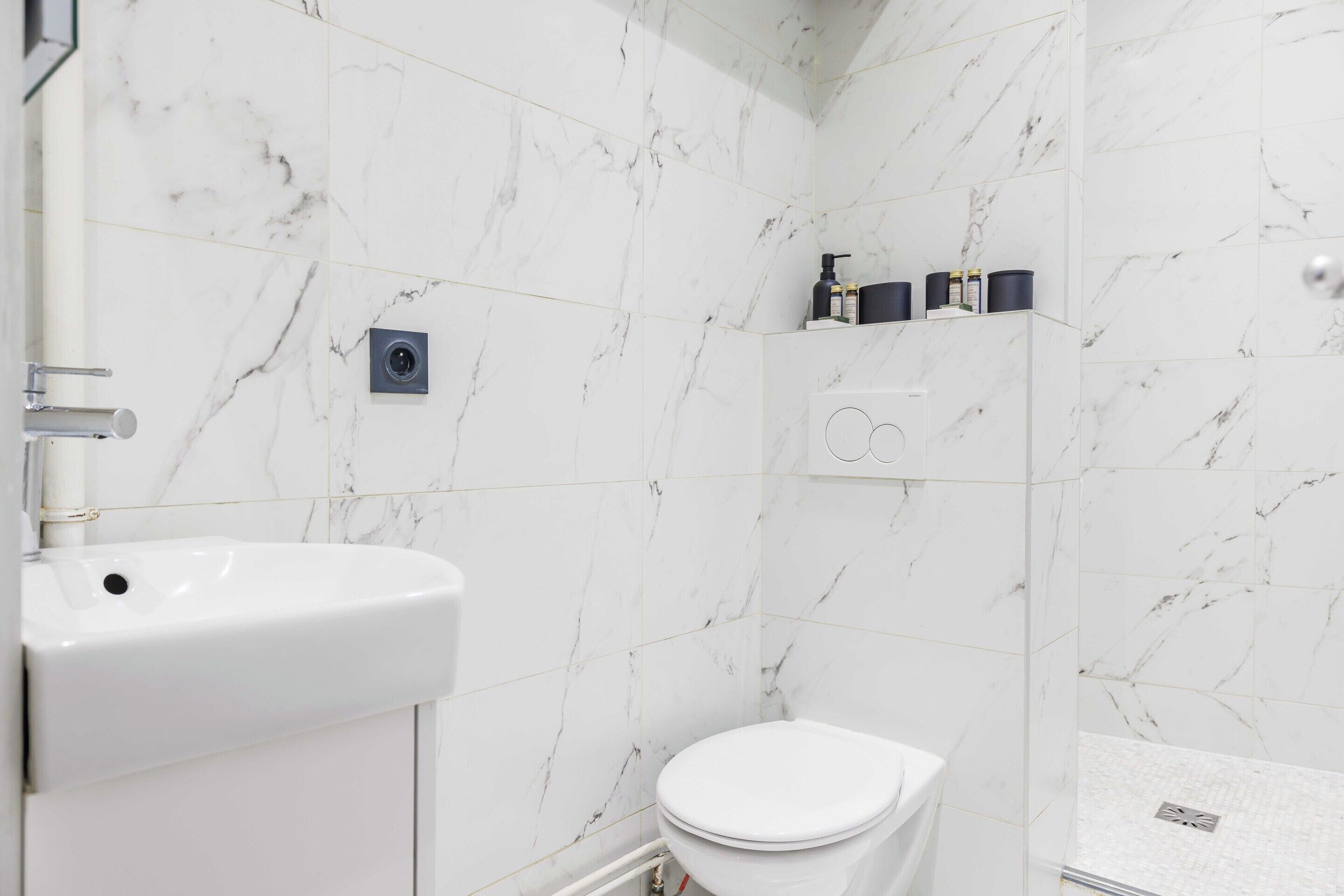 Ein Badezimmer mit weißen Marmorfliesen, einem weißen Waschbecken und einer Toilette.