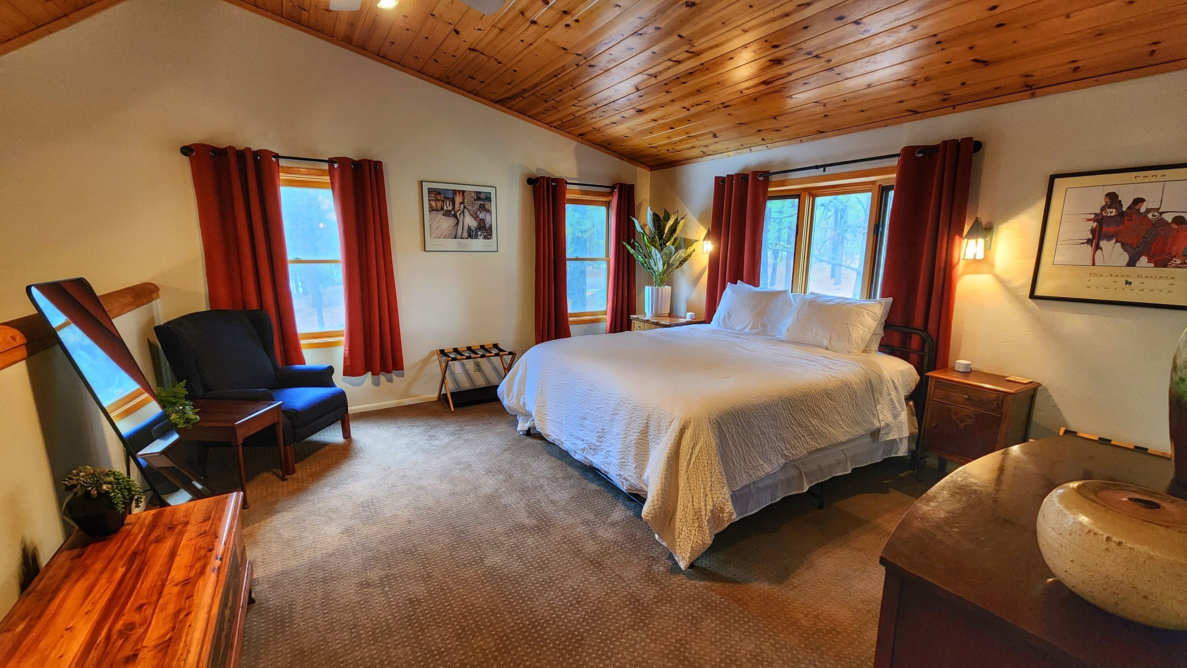 Une chambre à coucher avec un grand lit, une chaise, un bureau et une fenêtre avec des rideaux.