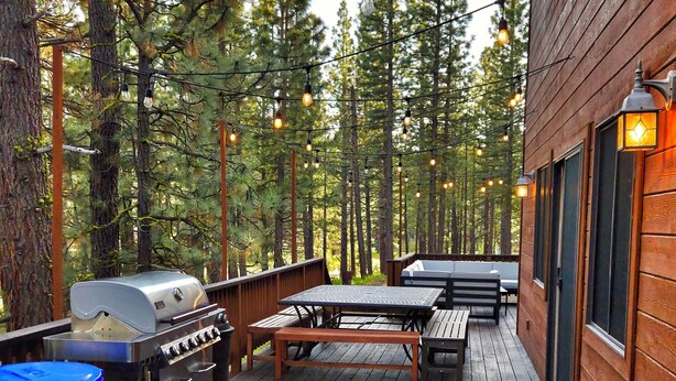 A wooden deck with a hot tub, outdoor seating, and string lights.