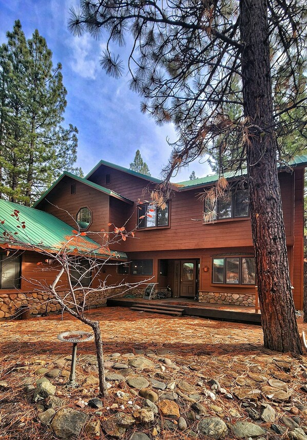 A two-story wooden house with a stone foundation, a green roof, and a stone patio.