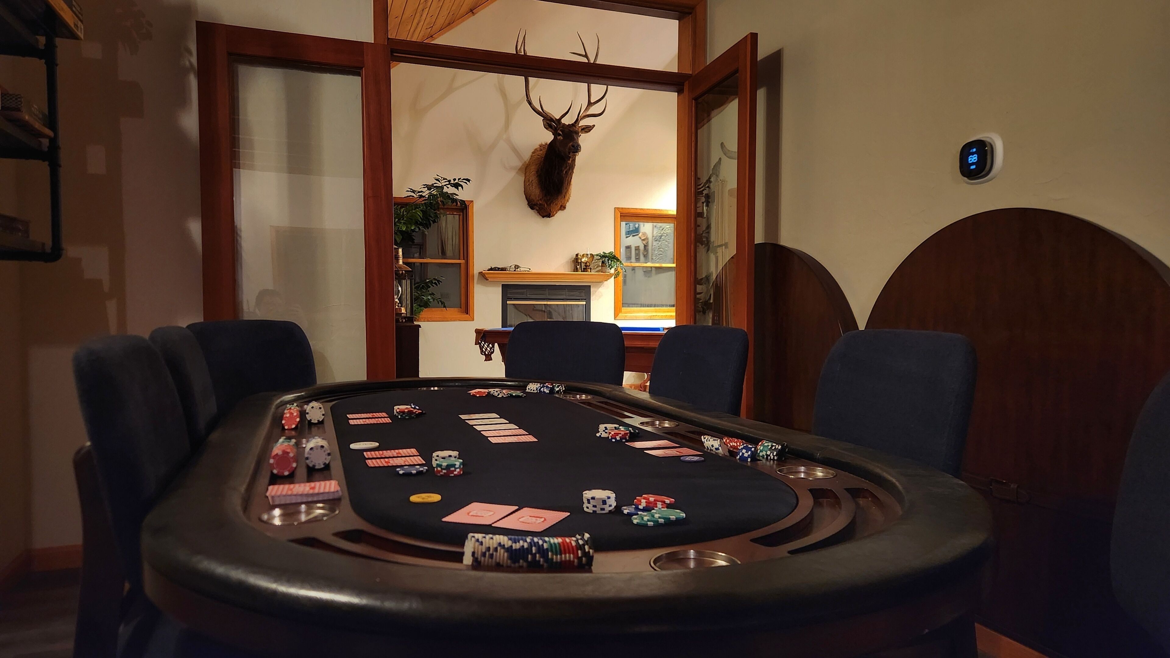 A poker table with chips and cards, a mounted deer head, and a fireplace in the background.