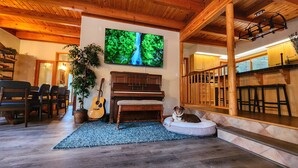 A cozy living room with a piano, a television, and a dog resting on a cushion.