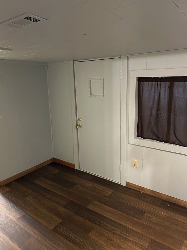 Ein Zimmer mit Holzboden, einer weißen Tür mit kleinem Fenster und einem braunen Vorhang.