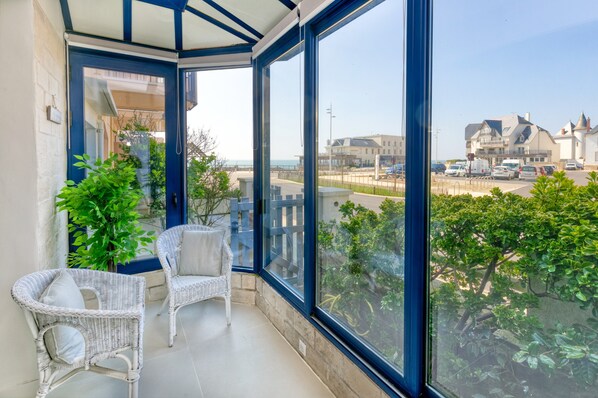 A balcony with wicker chairs, a glass door, and a view of the sea and buildings.