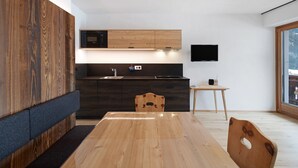 A modern kitchen with dark cabinetry, a wooden dining table, and a built-in microwave. - Apartment 'Pfaffingerhof Dolce Wood' with Mountain View, Shared Garden and Wi-Fi (Anterselva di Sotto BZ)