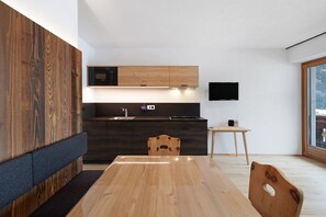 A modern kitchen with dark cabinetry, a wooden dining table, and a built-in microwave. - Apartment 'Pfaffingerhof Dolce Wood' with Mountain View, Shared Garden and Wi-Fi (Anterselva di Sotto BZ)