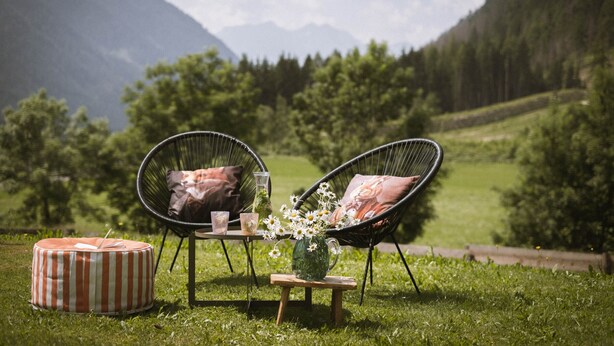 An outdoor seating area with two chairs, a small table, and a striped ottoman.