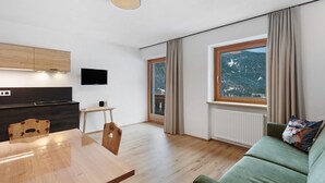 A modern living space with a dining table, sofa, and a large window with a mountain view.