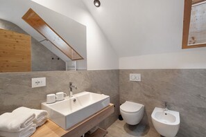 Un baño moderno con lavamanos, inodoro, bidé y un banco de madera.