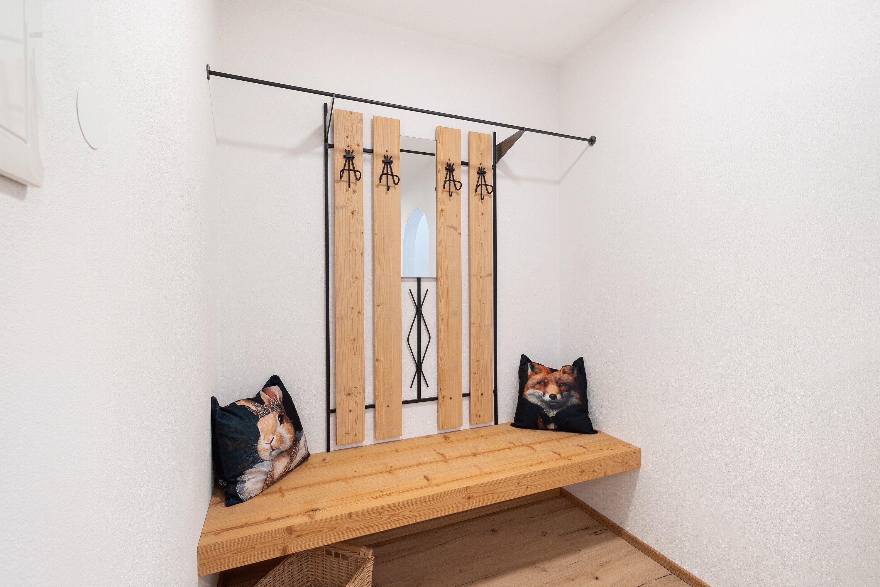 A corner of a room with a wooden bench, two pillows, and a wall-mounted rack with hooks.