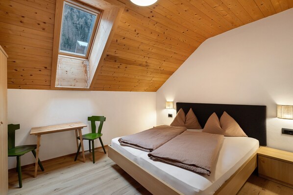 Un dormitorio con cama alta, escritorio y silla.