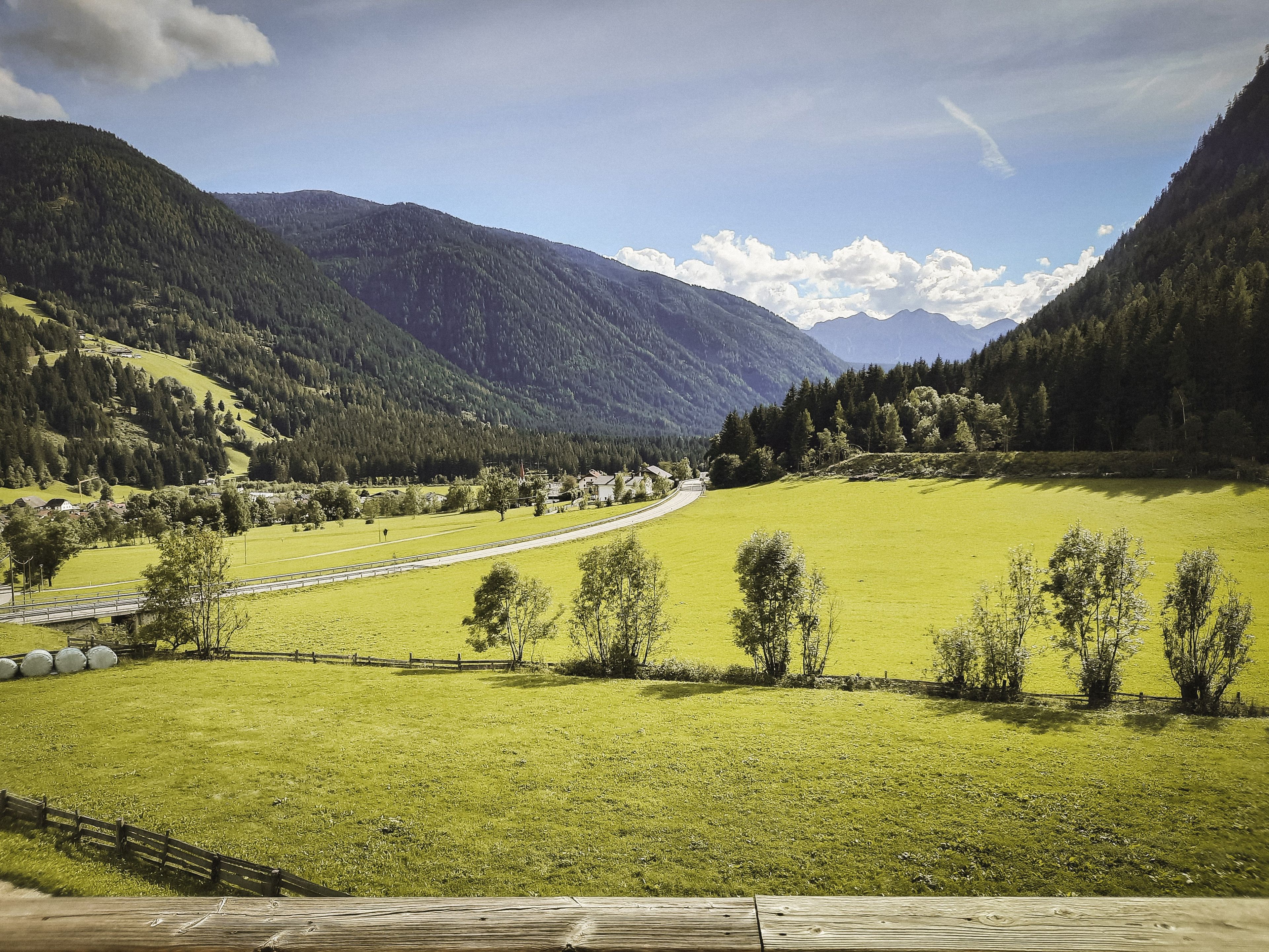 Een landelijk landschap met een weg, groene velden en bergen.