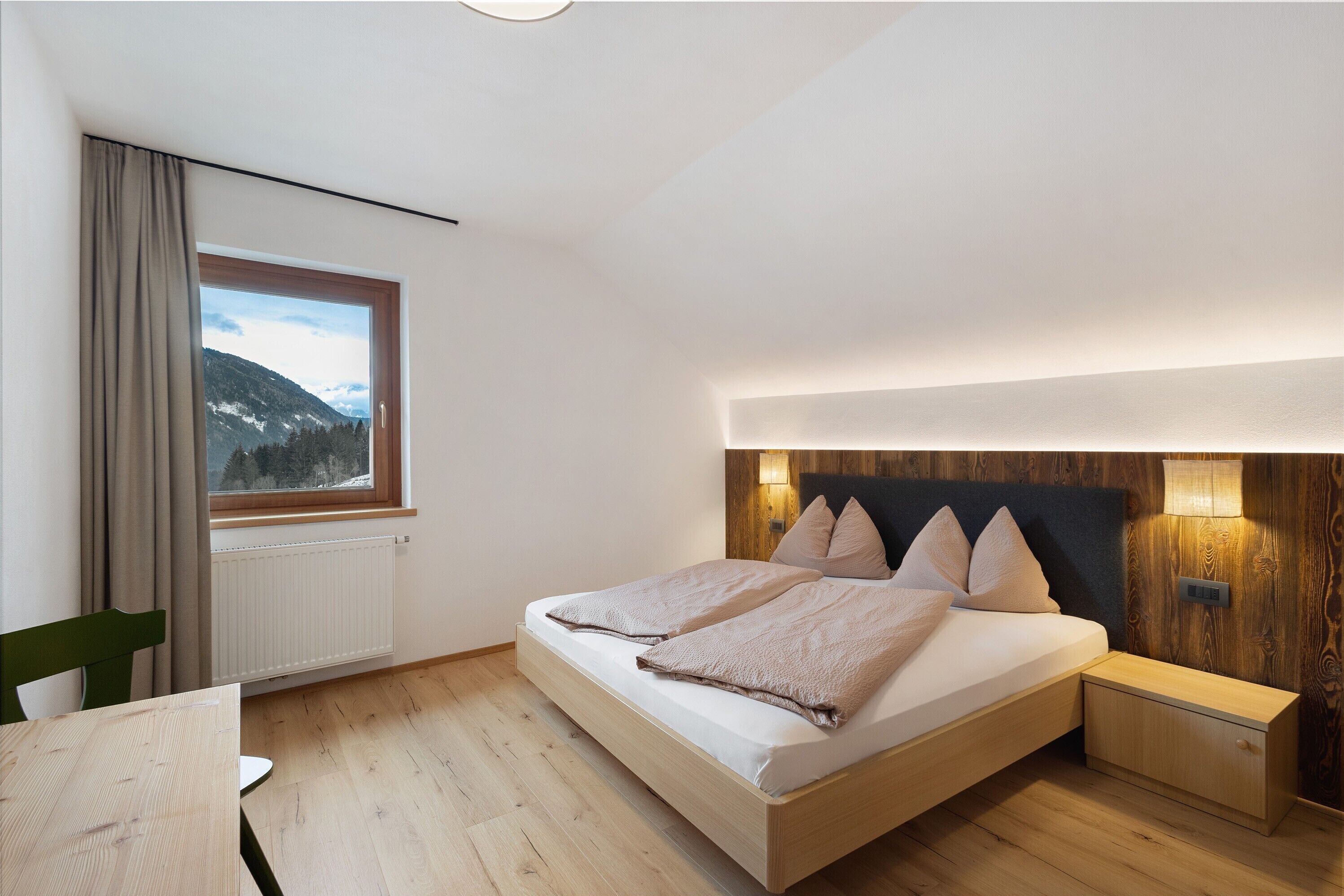 Camera da letto con un letto, comodino, lampada, finestra con tende e vista sulle montagne.