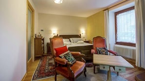 A hotel room with a bed, two armchairs, a small table, a wooden dresser, a rug, and a window with curtains. - Bed and Breakfast 'Il Pellegrino' with Mountain Views, Shared Garden and Wi-Fi (La Place)