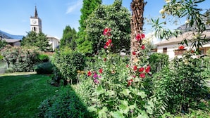 A garden with a variety of plants and flowers, a church with a clock tower, and a mountain in the background. - Bed and Breakfast 'Il Pellegrino' with Mountain Views, Shared Garden and Wi-Fi (La Place)