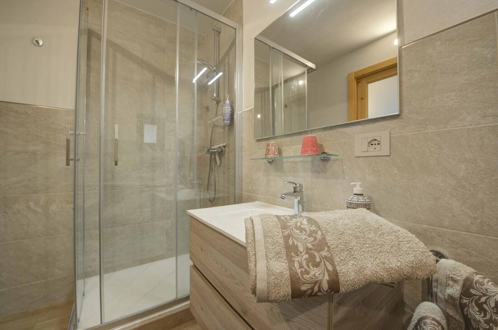 A modern bathroom with a glass shower enclosure, a wooden vanity, and a large mirror.