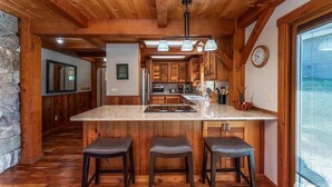 A kitchen with a large island, wooden beams, and a stone wall. - Wapato Point Escape: Private Hot Tub • Walk to Beach • Lake Views (Manson)
