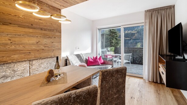 A modern living room with a wooden ceiling, a dining area with a table and chairs, a television, and a sliding glass door leading to an outdoor area. - Apartment 'Paradeis Apartments A20' with Mountain View, Balcony and Wi-Fi (Mühlbach)