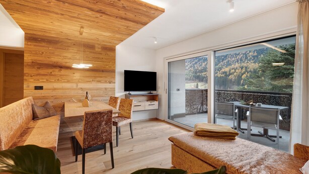 A modern living room with a wooden ceiling, a flat-screen TV, a dining area, and a balcony with a view of a forested area. - Apartment 'Paradeis Apartments A19' with Mountain View, Private Terrace and Wi-Fi (Mühlbach)