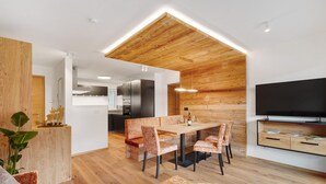 A modern kitchen with wooden ceiling, a dining area with patterned chairs, and a flat-screen TV on the wall. - Apartment 'Paradeis Apartments A19' with Mountain View, Private Terrace and Wi-Fi (Mühlbach)