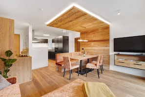 Una cucina moderna con soffitto in legno, un'area pranzo con sedie a fantasia e una TV a schermo piatto appesa al muro.