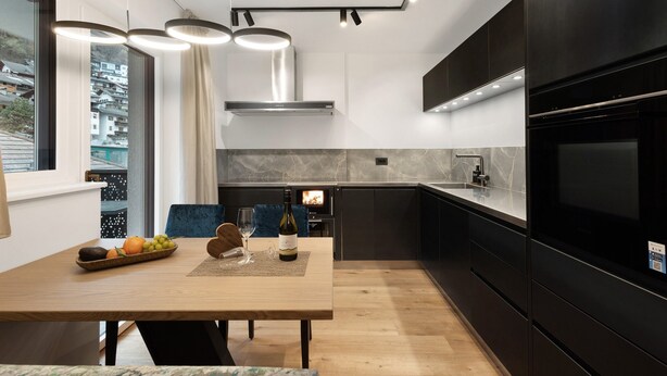 A modern kitchen with a dining area, a built-in stove, and a large black refrigerator. - Apartment 'Paradeis Apartments A18' with Mountain View, Private Terrace and Wi-Fi (Mühlbach)