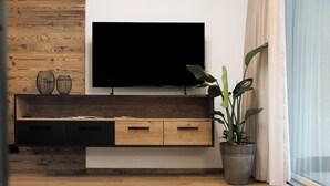 A modern living room with a wooden wall, a flat-screen TV, a wooden cabinet, and a potted plant. - Apartment 'Paradeis Apartments A18' with Mountain View, Private Terrace and Wi-Fi (Mühlbach)