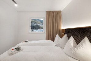 A hotel room with a bed, a window with a view of buildings, a headboard, and a curtain.