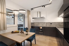 A modern kitchen with a built-in oven, a dining table with chairs, and a view of the outside.